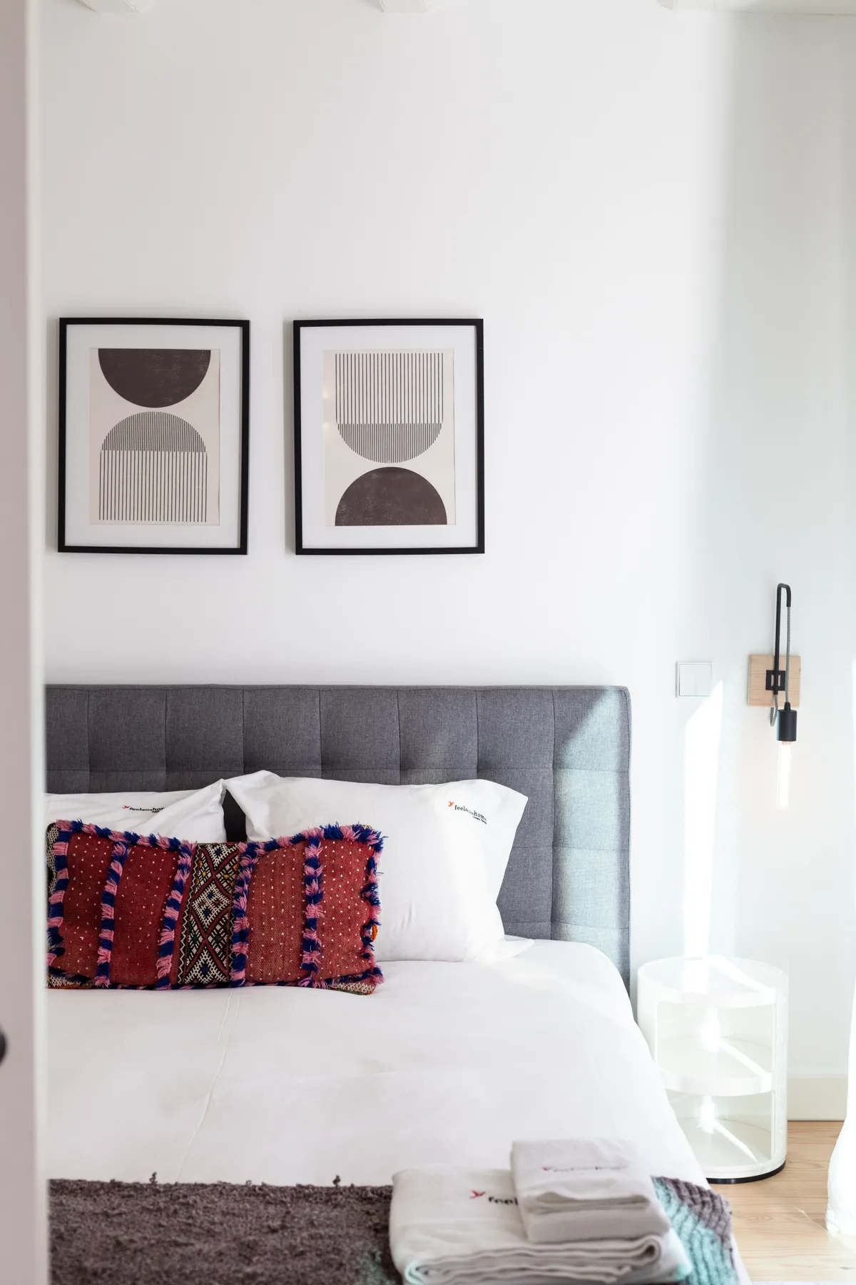 Un dormitorio con una cama bien arreglada, cojines decorativos y láminas enmarcadas.