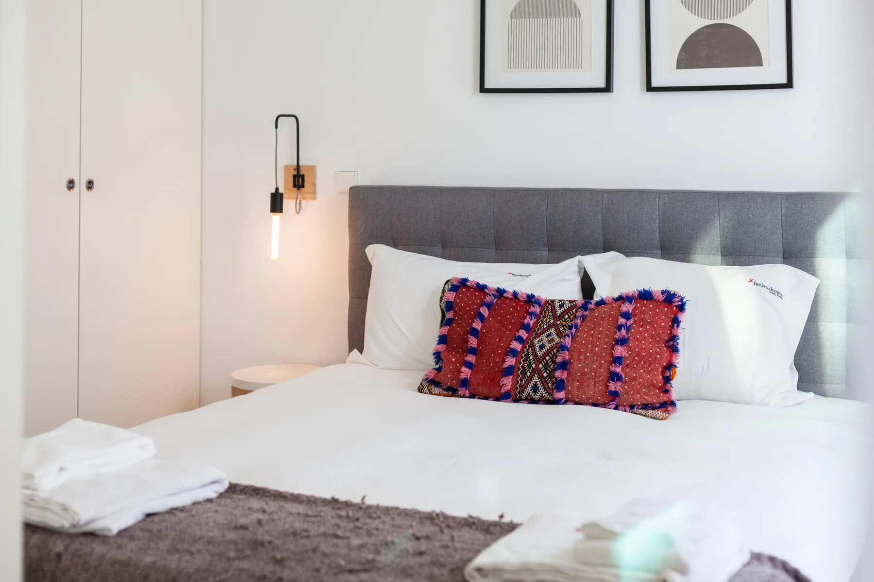 Un dormitorio con una cama bien arreglada, cojines coloridos y láminas enmarcadas.