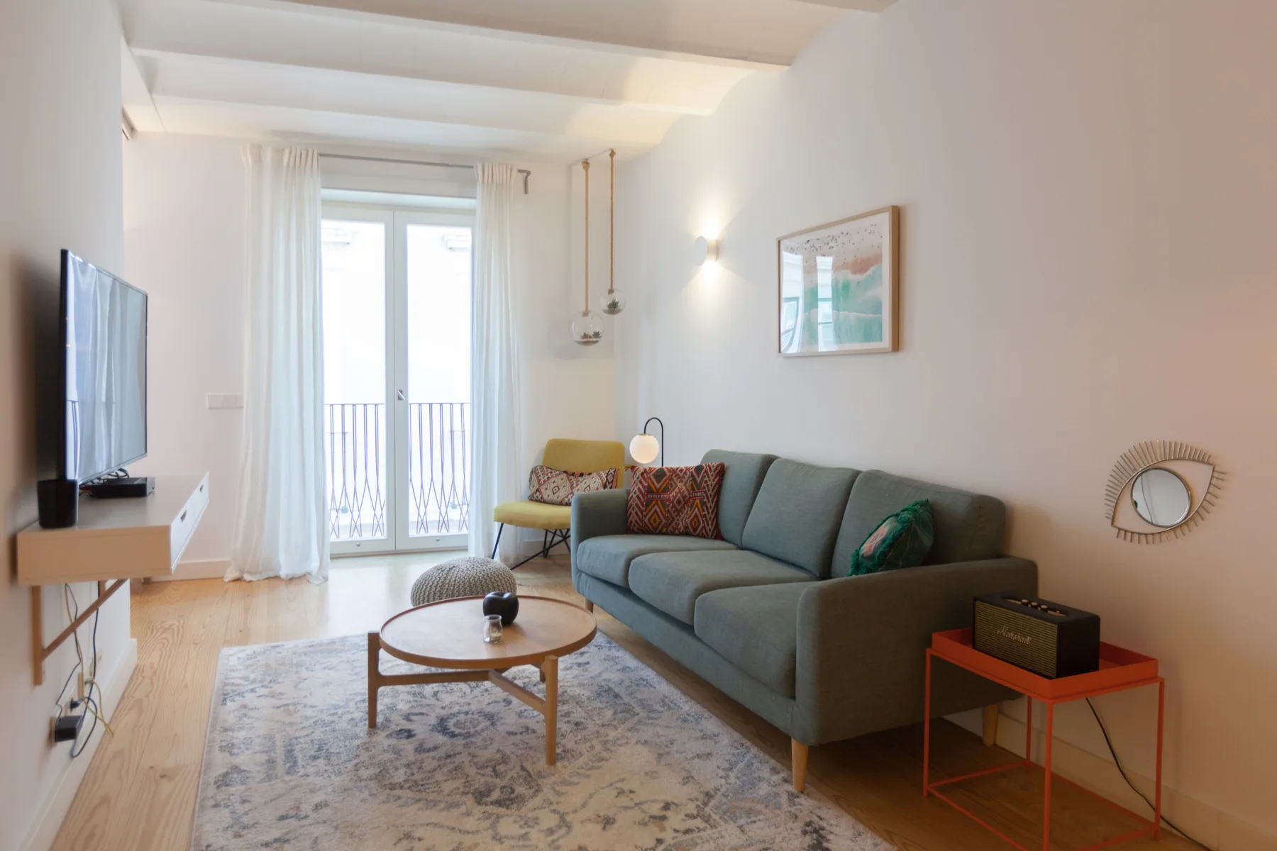 Una sala luminosa con asientos, una mesa de centro y puertas de vidrio que dan a un balcón.