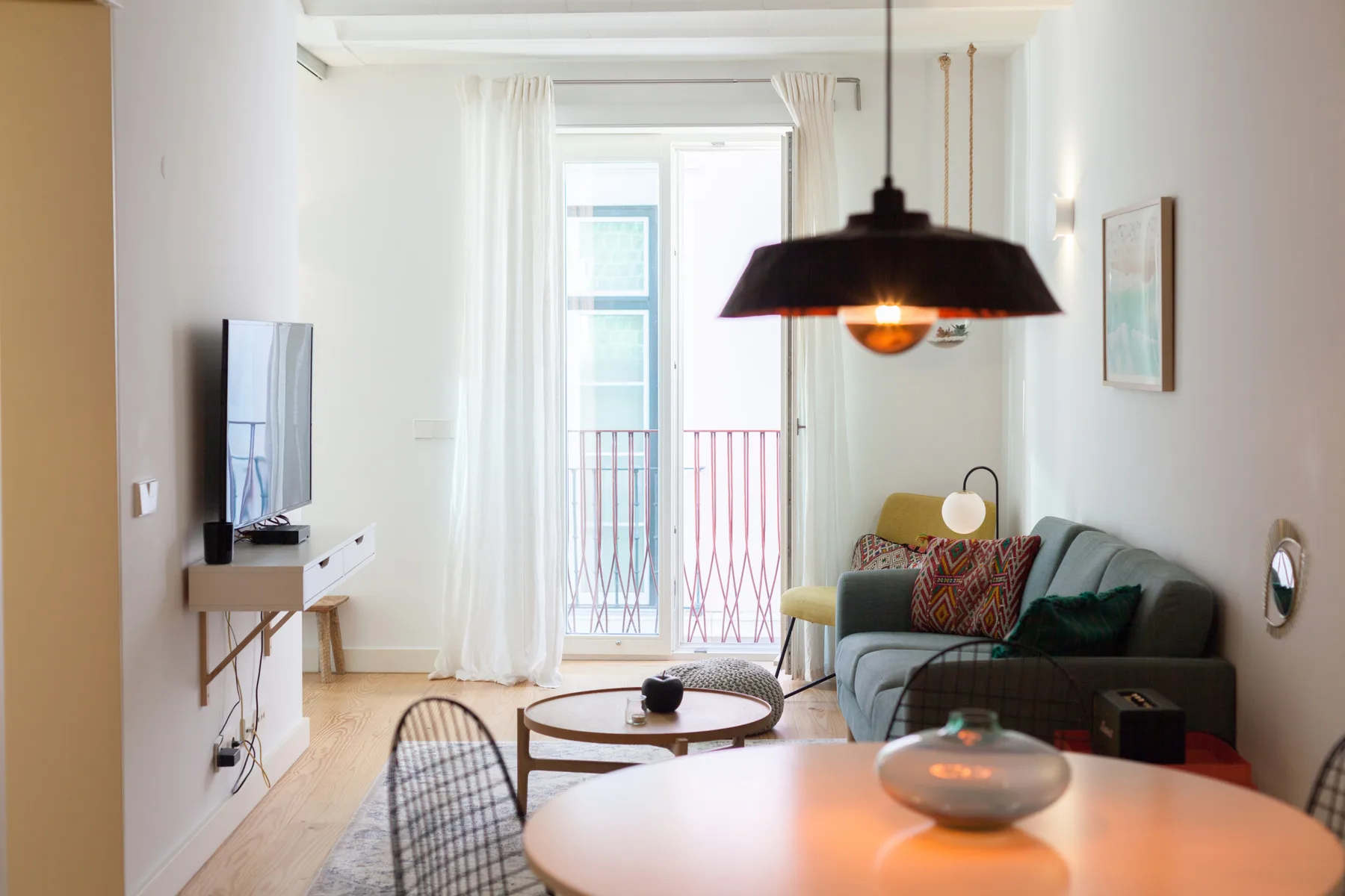 Una sala luminosa con asientos, un televisor y puertas de vidrio que dan a un balcón.