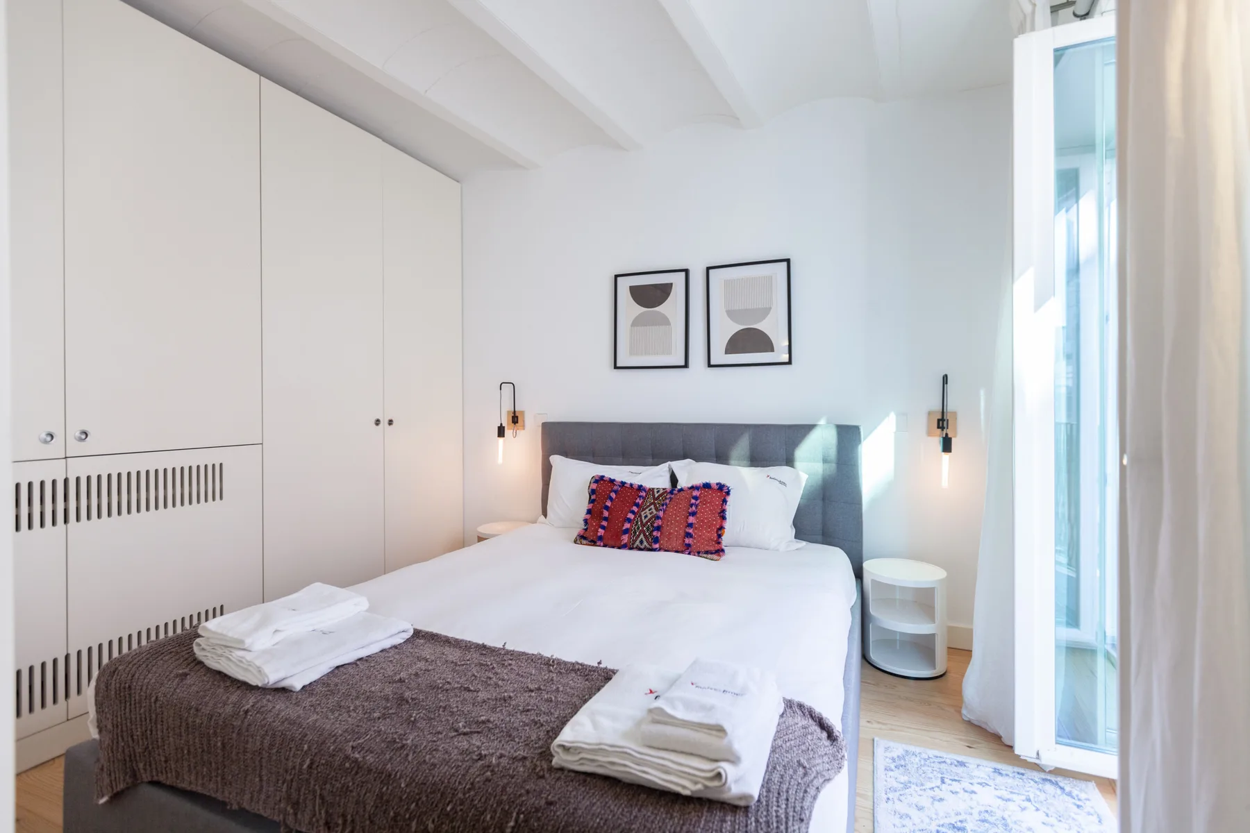 Un dormitorio luminoso con cama doble, cuadros enmarcados y una ventana alta.