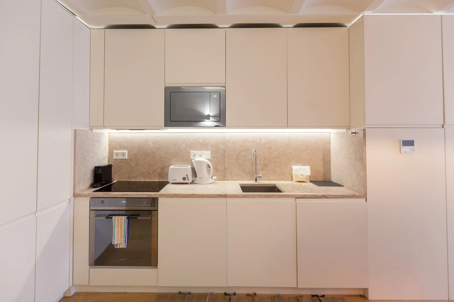 Una cocina compacta con armarios claros, encimera y electrodomésticos integrados.