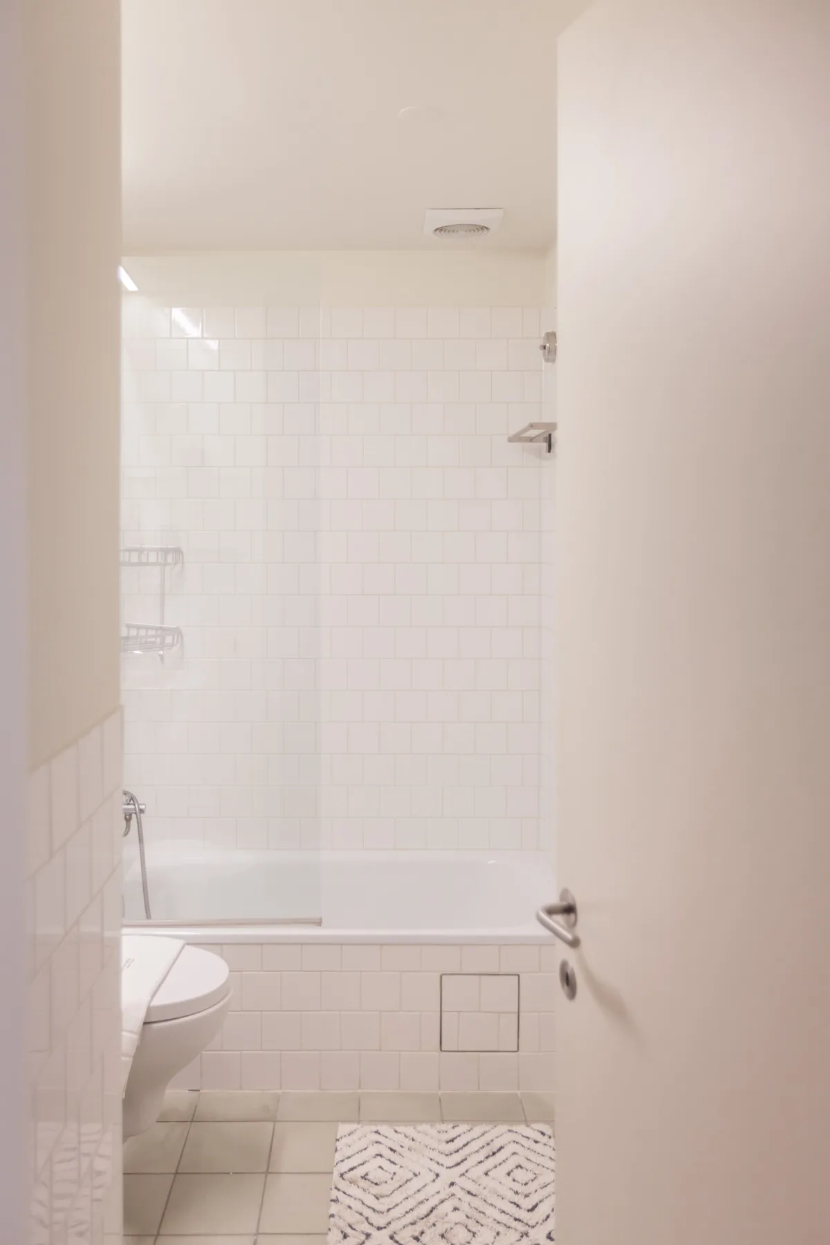 Un baño alicatado con bañera, inodoro y una alfombrilla estampada.
