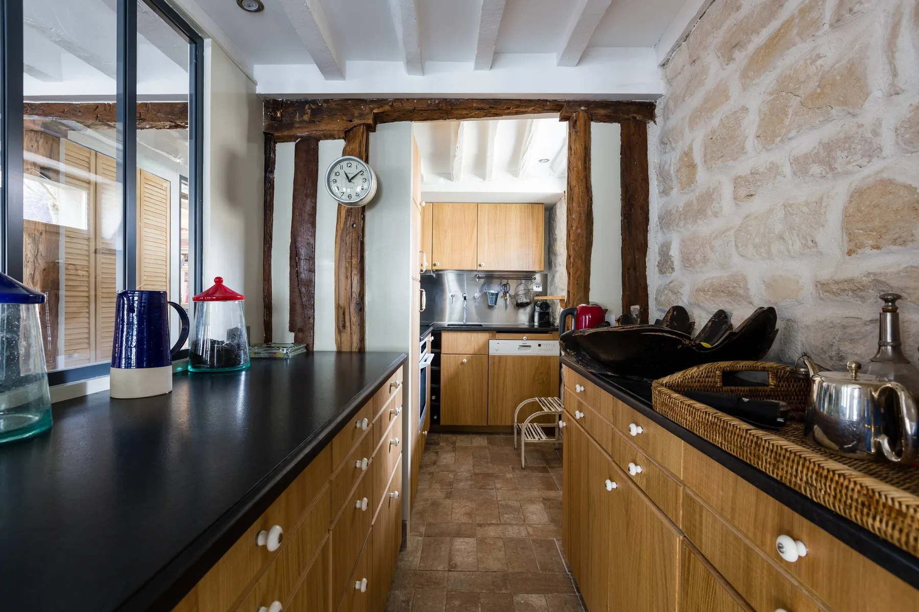 Una cocina estrecha con armarios de madera, encimeras oscuras y paredes de piedra vista.