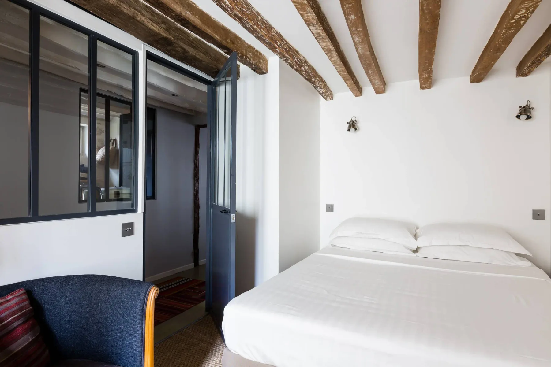 Un dormitorio luminoso con una cama blanca bajo vigas de madera expuestas.