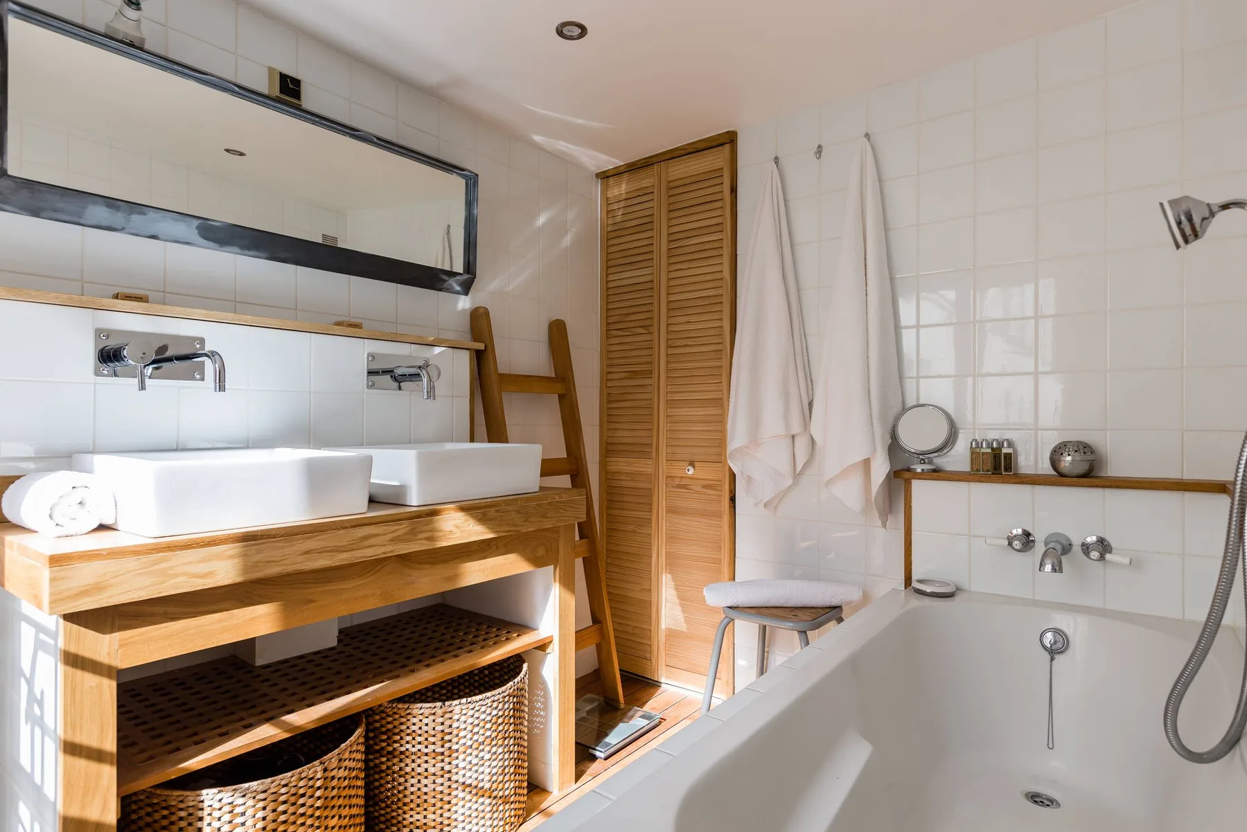 Un baño alicatado con mueble de madera, bañera y toallas colgadas.