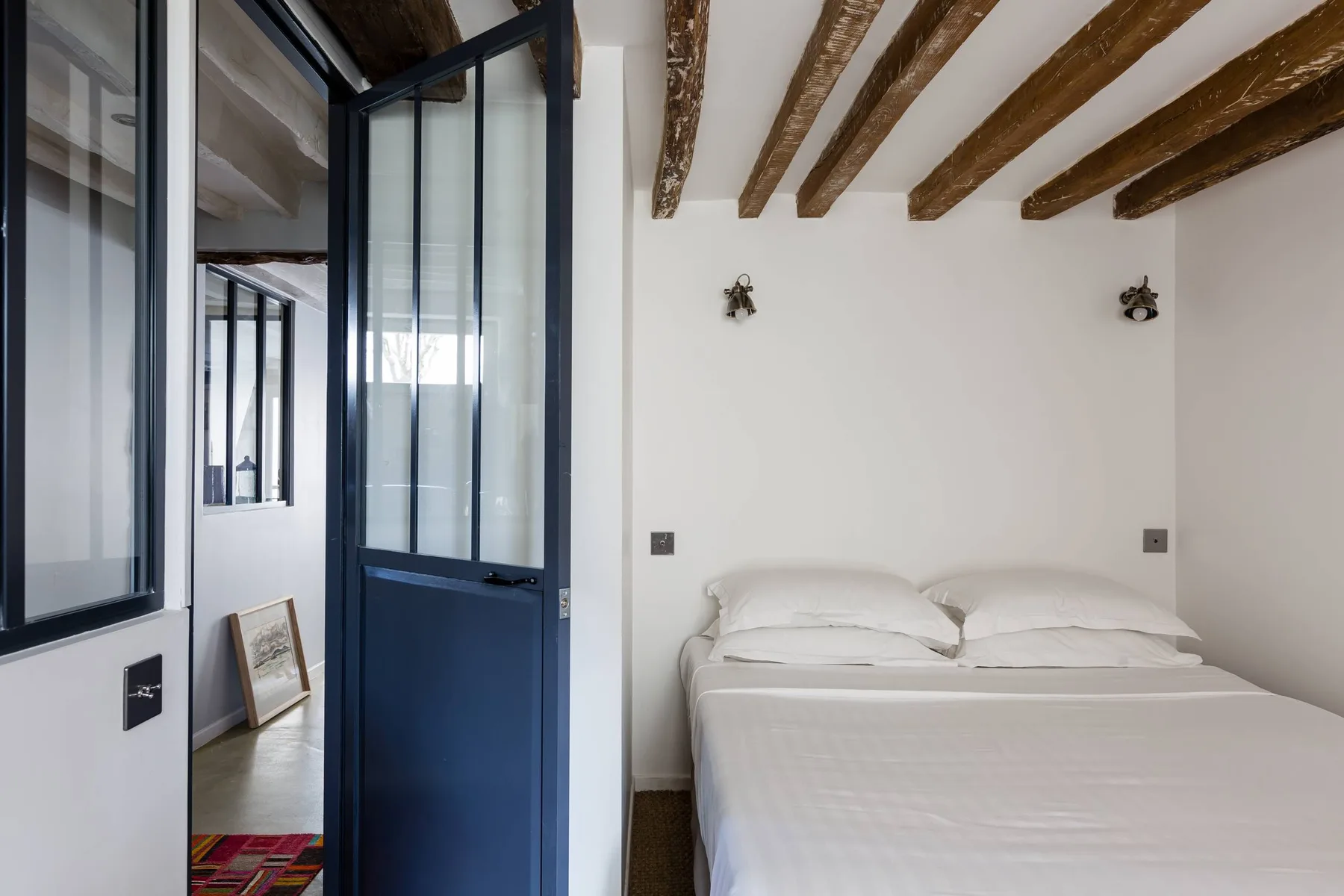 Un dormitorio con una cama bajo vigas de madera expuestas en el techo.