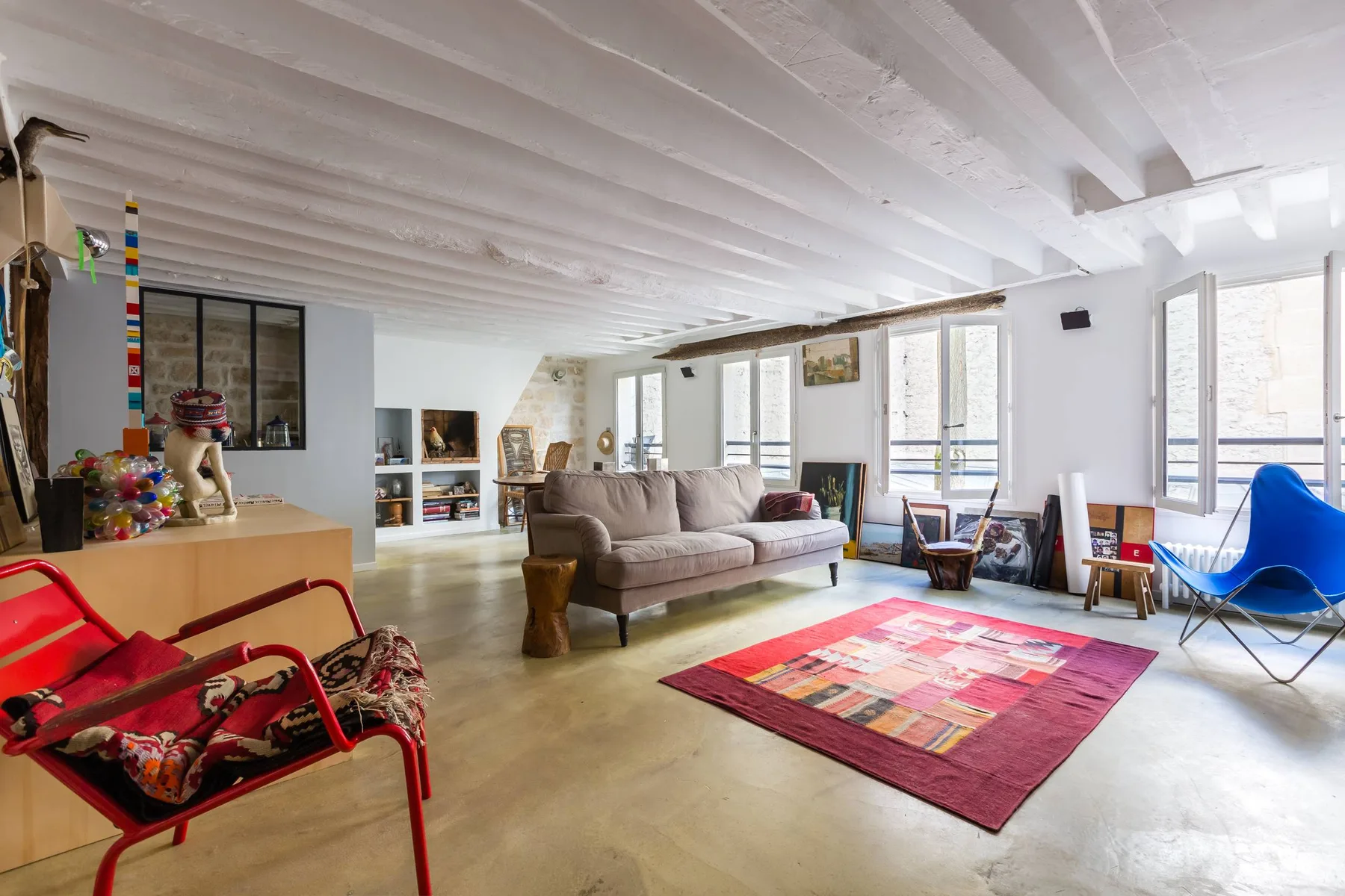 Una sala luminosa con sofá, alfombra colorida y ventanas amplias.
