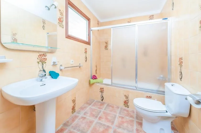 A tiled bathroom with a sink, toilet, and frosted-glass shower enclosure.