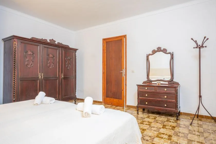 A bedroom with a large bed, a wooden wardrobe, and a dresser with a mirror.