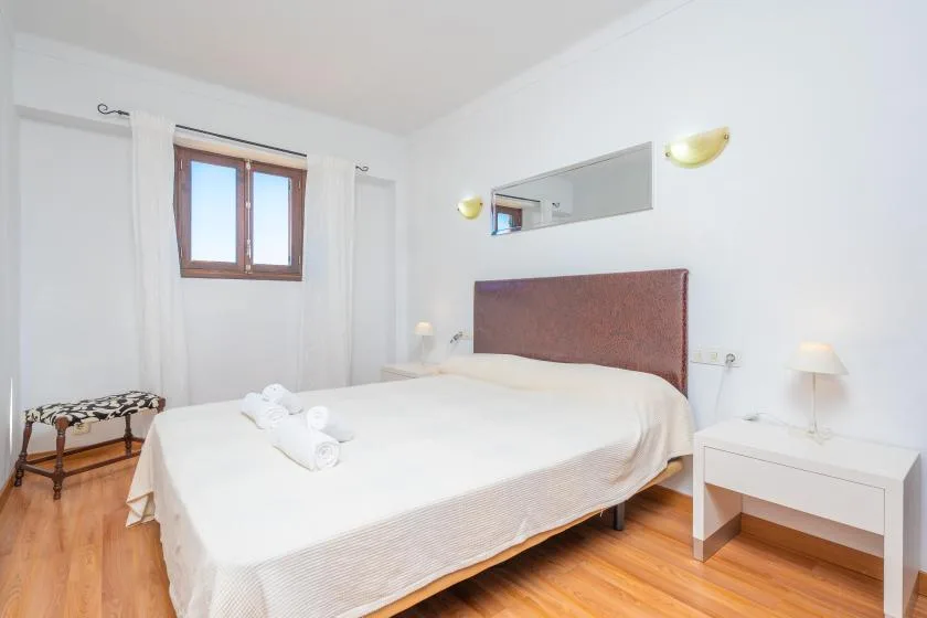 A bright bedroom with a bed, a window, and a small bedside table.