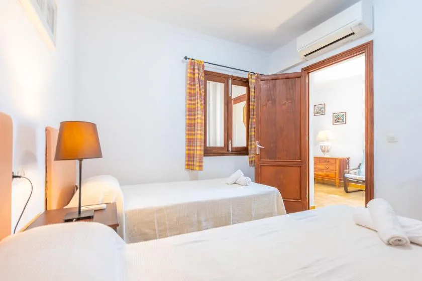 A bright bedroom with two beds, a wooden door, and a window with plaid curtains.