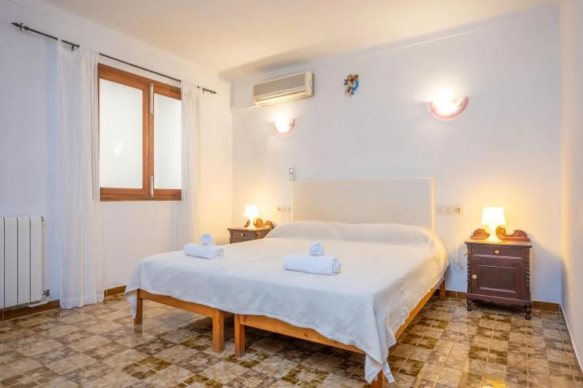 A bright bedroom with a neatly made bed and a window with curtains.
