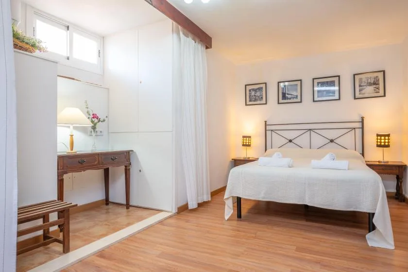 A bright bedroom with a bed, framed pictures, and a writing desk.
