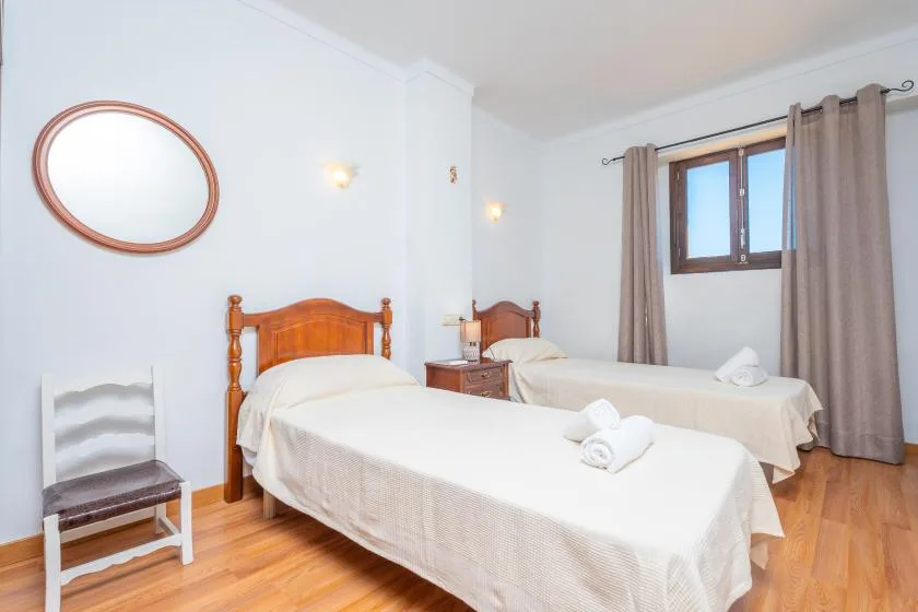 A bright bedroom with two beds, a small table, and a curtained window.