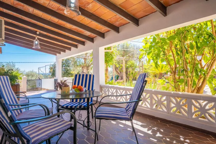A covered outdoor patio with striped seating and a table overlooks a leafy garden.