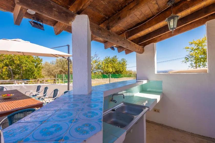 An outdoor kitchen with a tiled counter and sink overlooks a patio and open landscape.