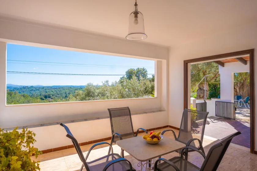 A covered patio dining area opens onto a green landscape through a wide window.