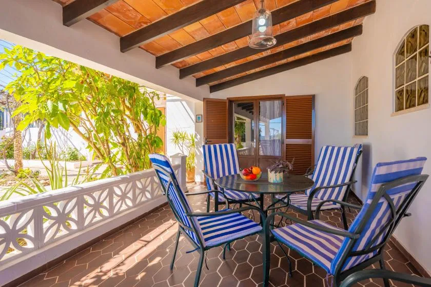 A covered patio has a glass table and blue-and-white striped seating.