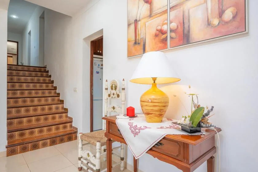 A hallway with a patterned staircase and a wooden console table beneath colorful artwork.