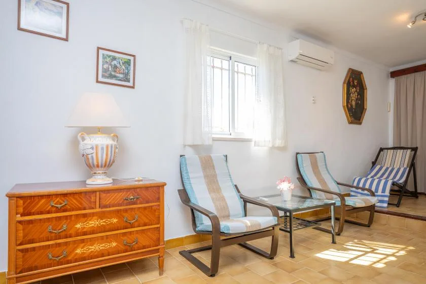 A bright sitting room has striped seating arranged around a glass coffee table.