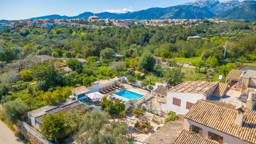 Aerial view of a swimming pool and terracotta-roofed buildings amid green hills.
