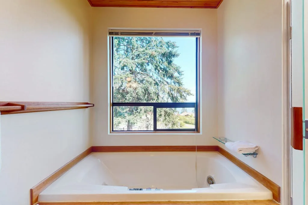 A bathroom with a built-in bathtub beneath a window overlooking trees.