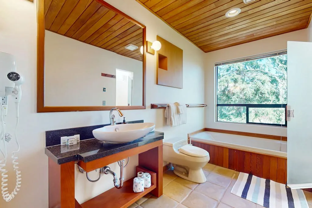 A bathroom with a sink, toilet, and bathtub beneath a large window.