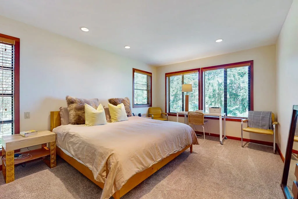 A bedroom with a large bed, broad windows, and a seating area.