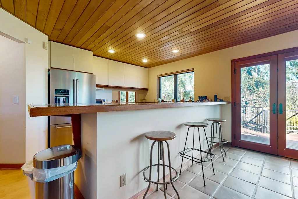 A kitchen with a breakfast bar and stools beside glass doors.