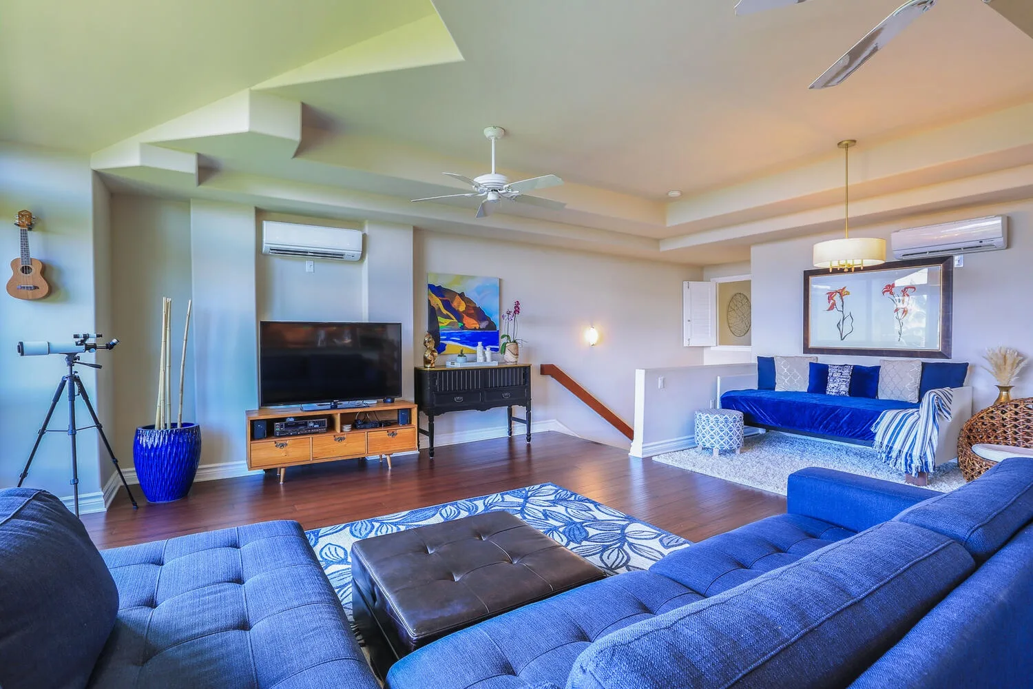 A bright living room with blue seating, a television, and a ceiling fan.