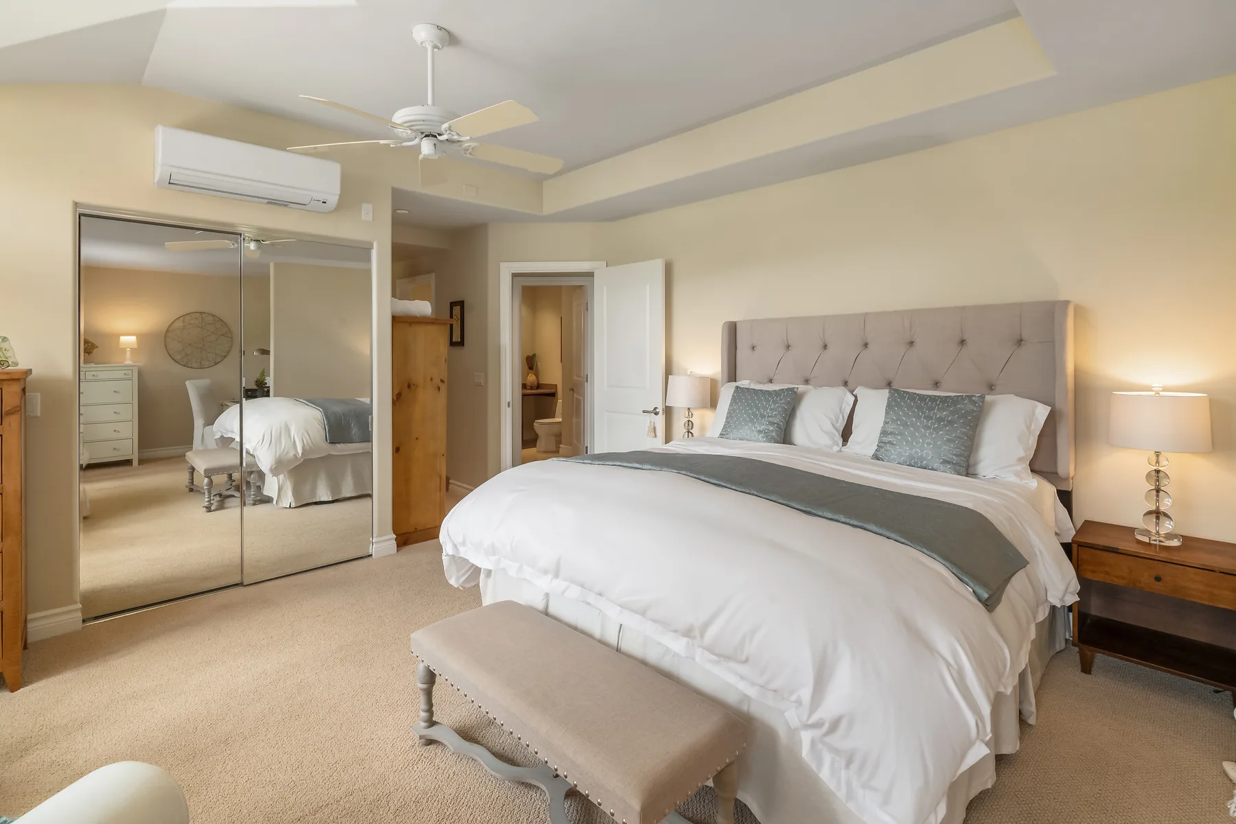 A bedroom with a large bed, mirrored wardrobe, and ceiling fan.