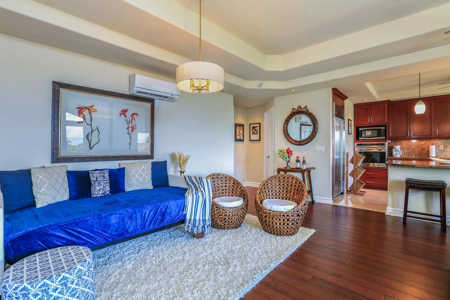A living room with blue seating, two wicker chairs, and an open kitchen.