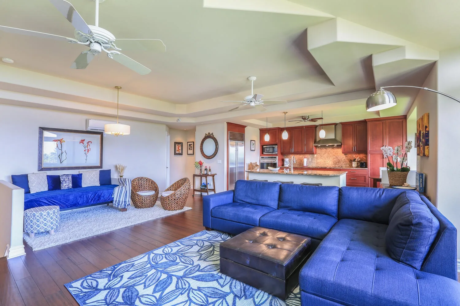 A living room with blue seating and an open kitchen in the background.