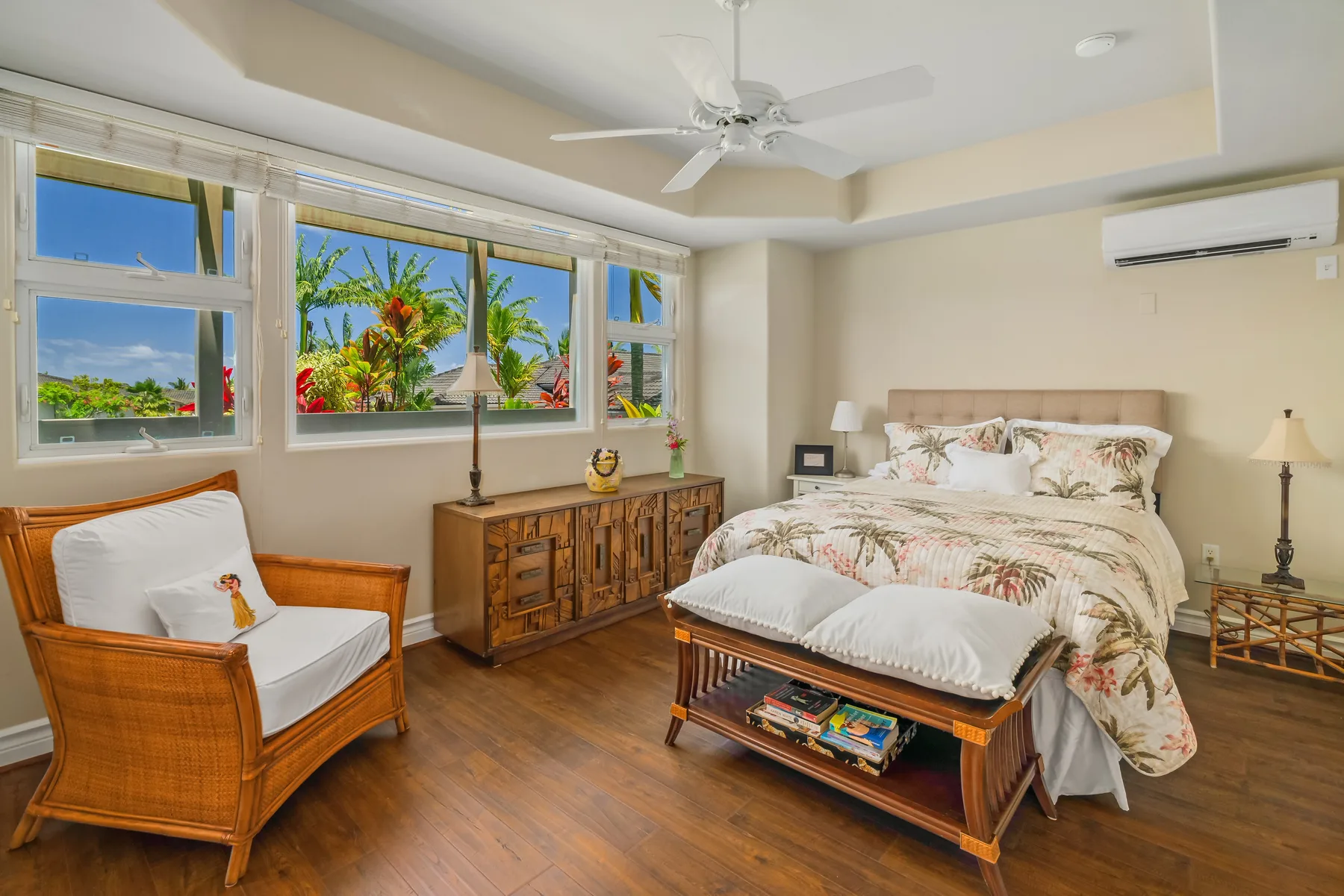 A bedroom with a bed, wooden seating, and large windows overlooking greenery.