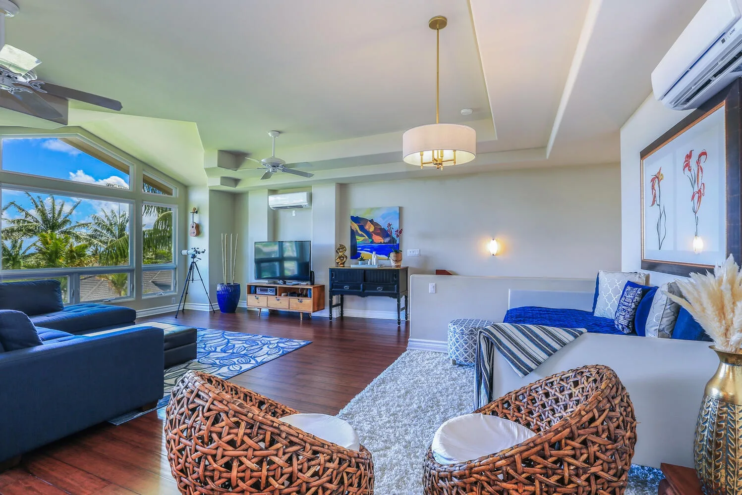 A bright living room with seating, a television, and large windows overlooking palm trees.
