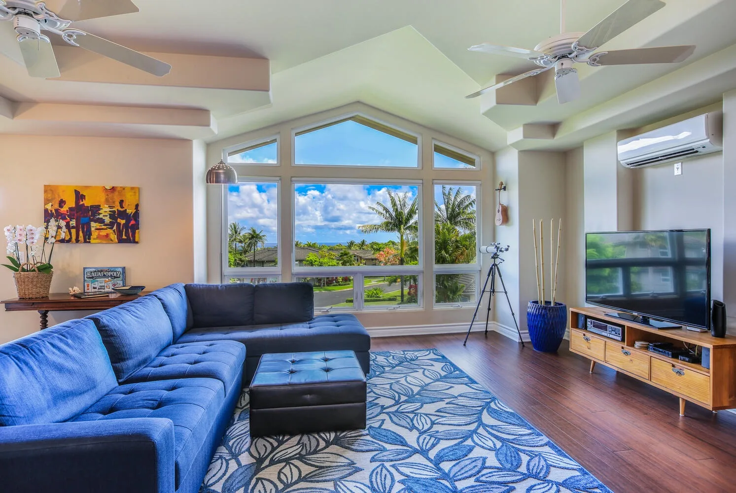 A living room with blue seating, a television, and large windows overlooking greenery.