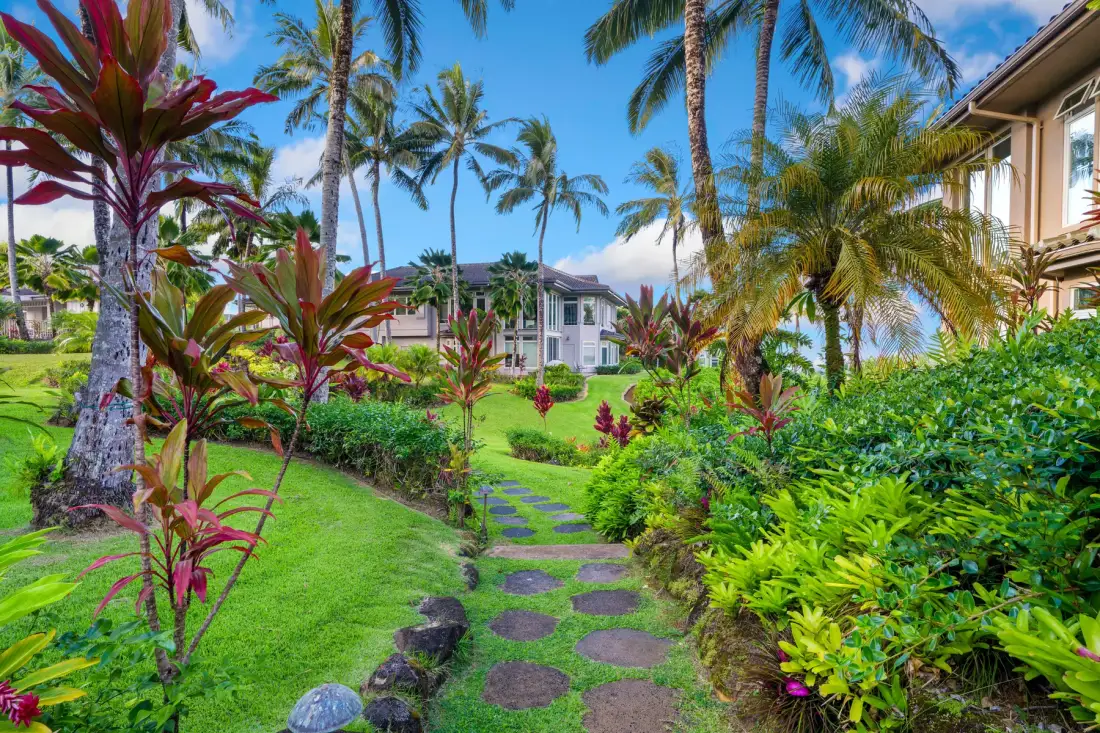 A landscaped garden path winds through tropical plants and palm trees.