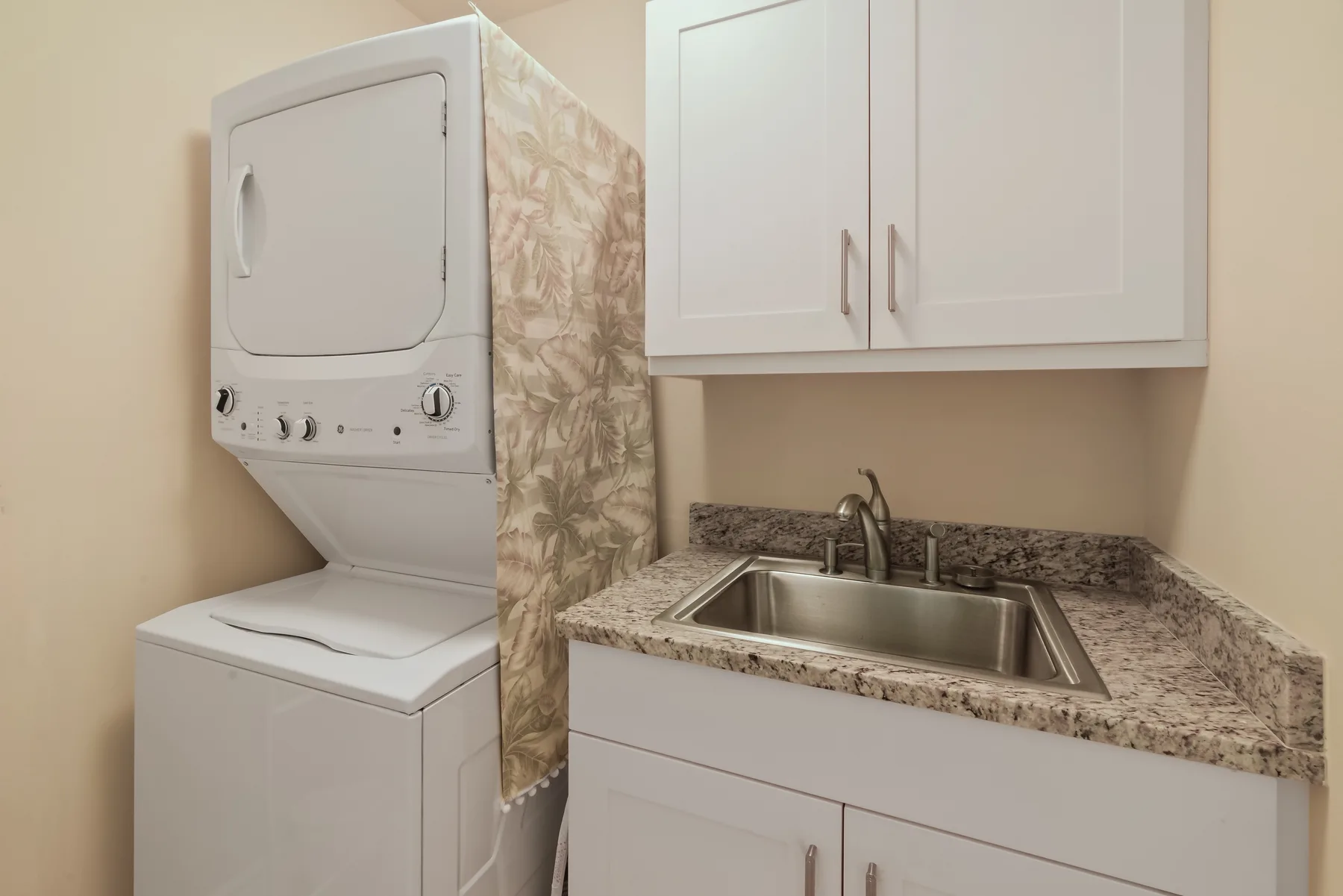 A laundry area with a stacked washer and dryer beside a sink and cabinets.