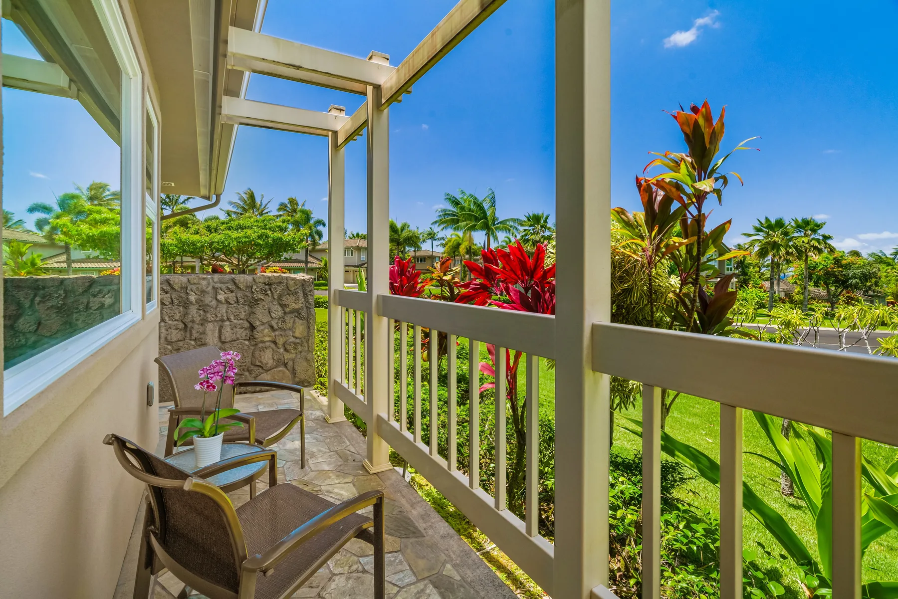 A covered outdoor balcony with seating overlooks a lush tropical garden.