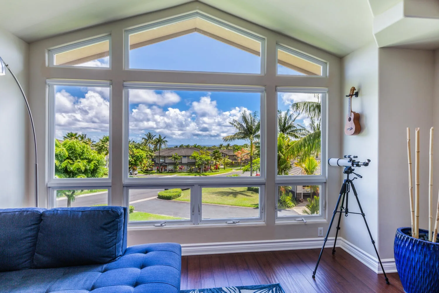 A bright living room with large windows overlooking palm trees and greenery.