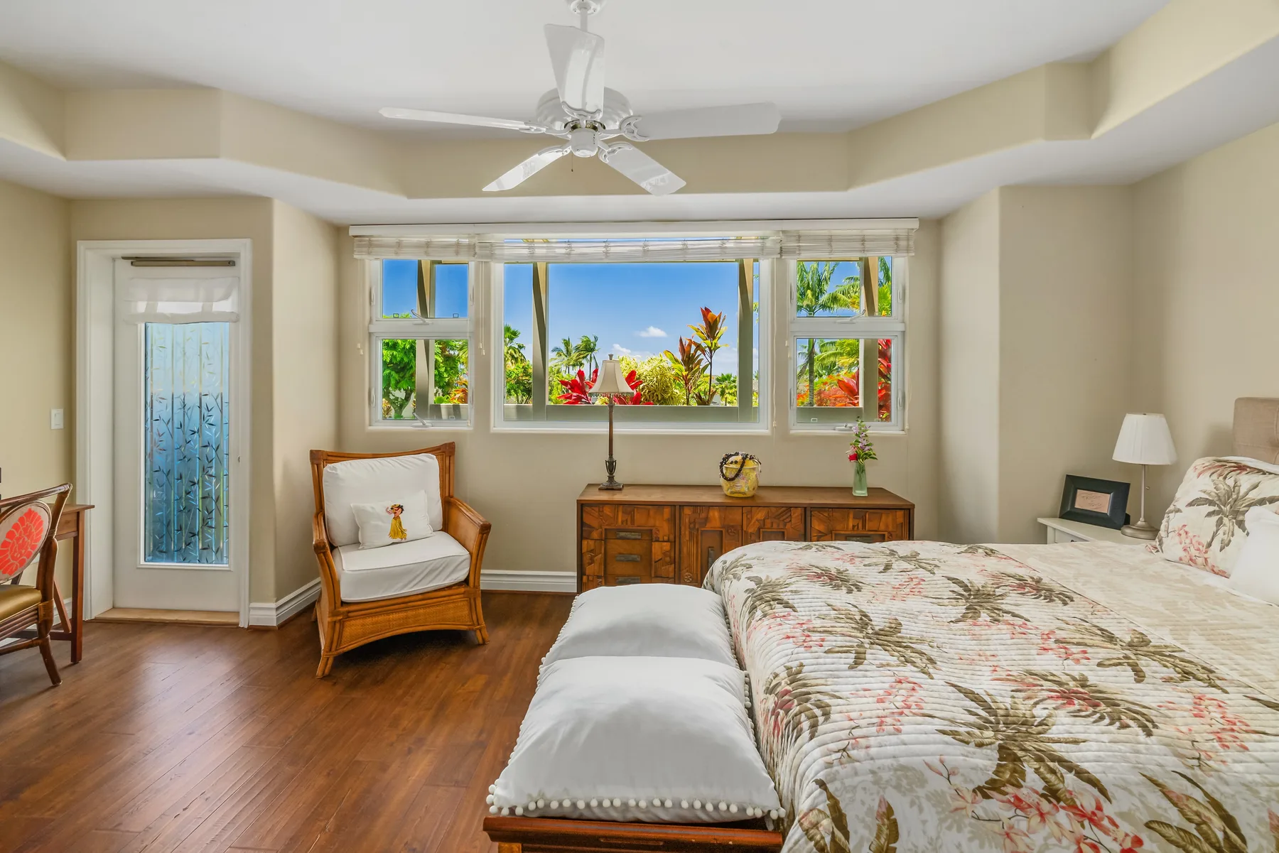 A bright bedroom with a bed, an armchair, and windows overlooking greenery.