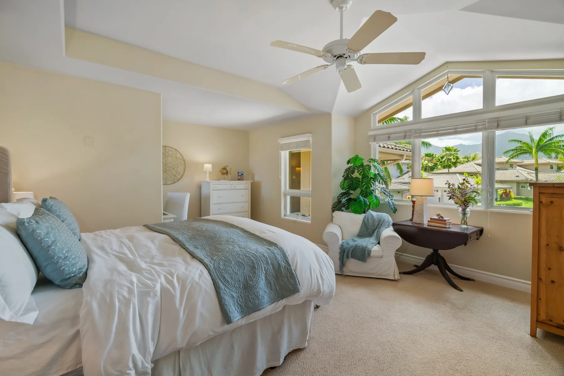 A bright bedroom with a bed, an armchair, and wide windows overlooking greenery.