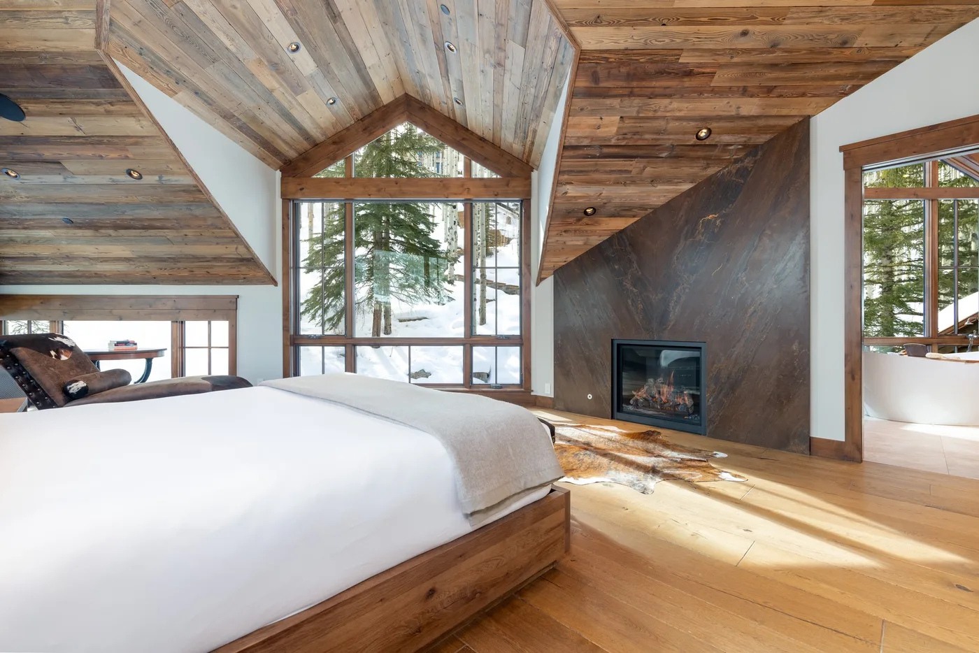 A bedroom with a large bed, wood-paneled ceiling, and fireplace.