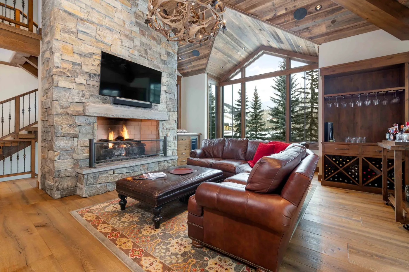 A rustic living room with leather seating, a stone fireplace, and large windows.