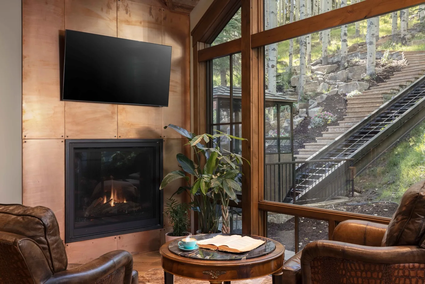 A living room with a fireplace, seating, and large windows overlooking outdoor steps.