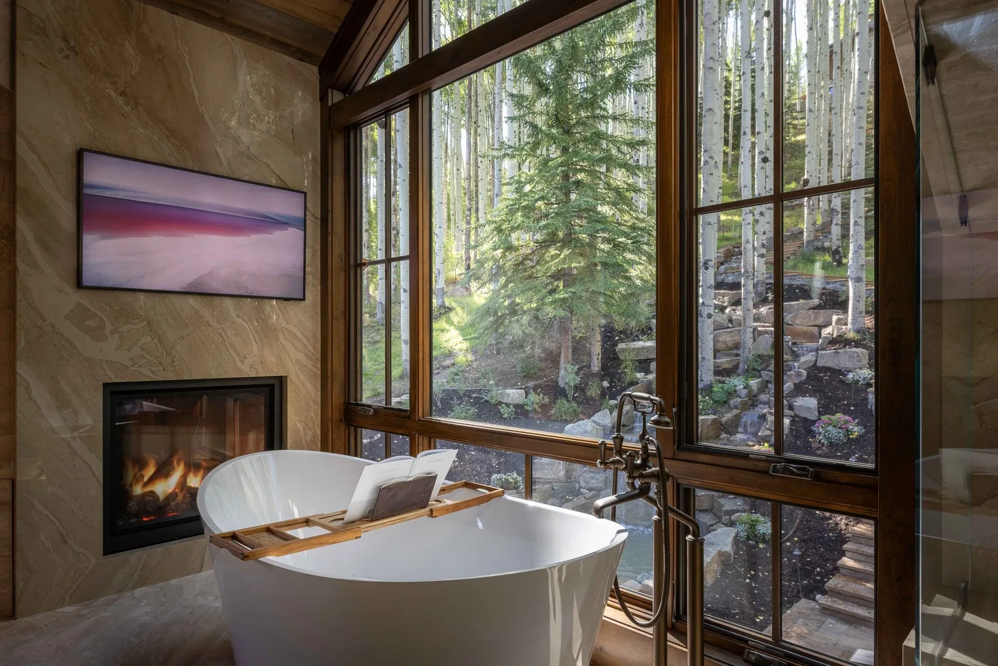 A bathroom with a freestanding tub beside large windows overlooking trees.