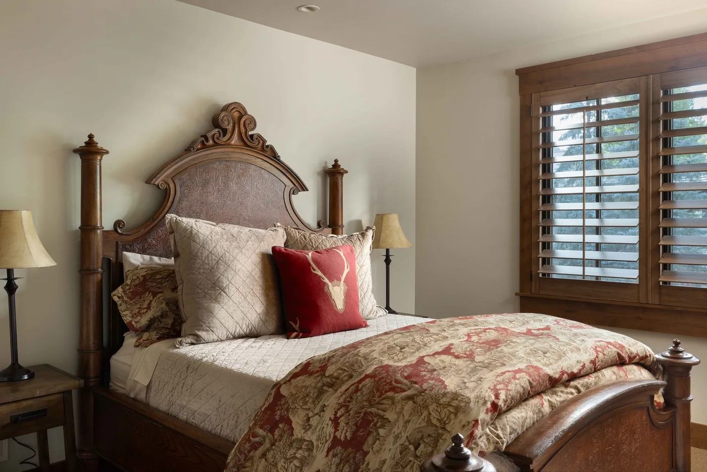 A bedroom with a wooden bed, patterned bedding, and a window with wooden blinds.
