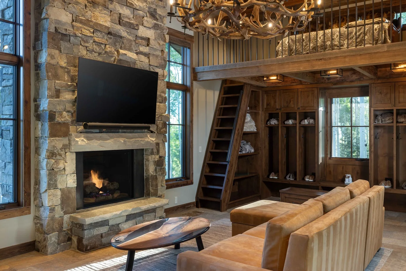 A rustic living room with a stone fireplace, large television, and seating.