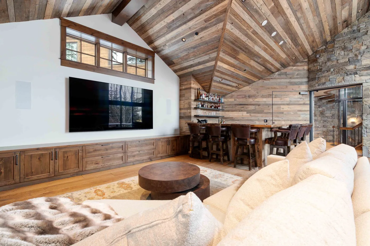 A rustic living room with a large television, dining table, and exposed timber ceiling.